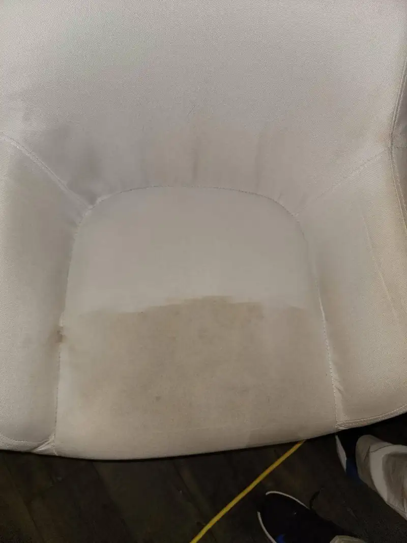 Real job photo: close-up of a cream upholstered chair seat, the upper half cleaned and pale and the lower half still gray-brown.